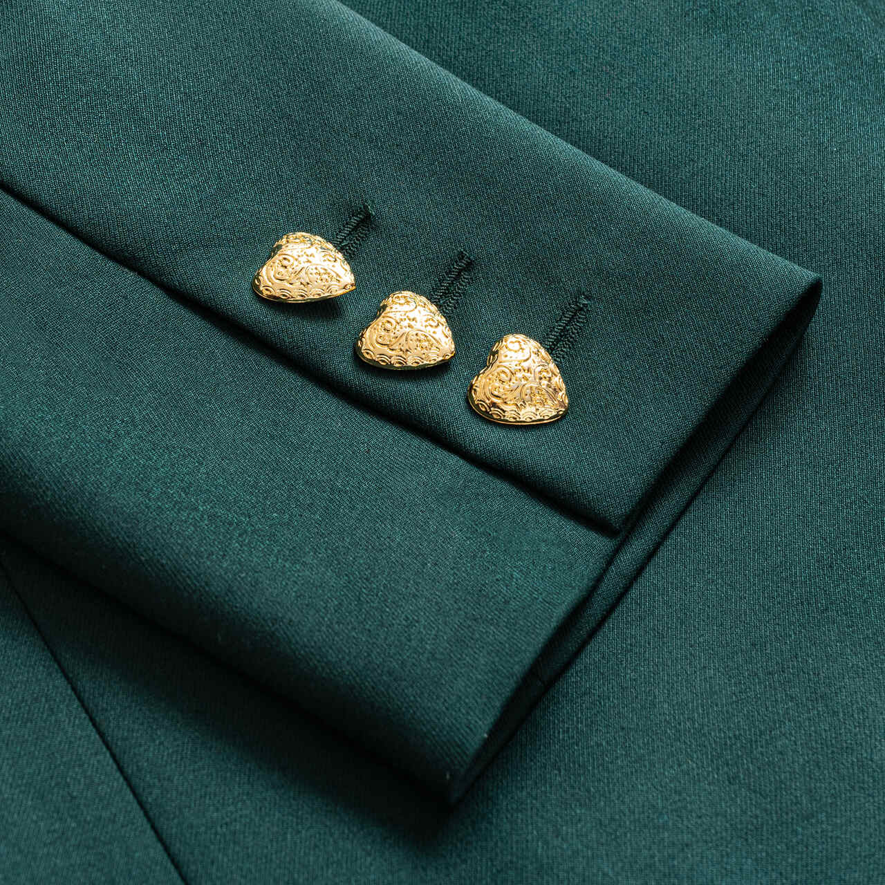 Aleksandra Markowska – detal złotych guzików w kształcie serca na rękawie zielonej marynarki, luksusowy akcent w kolekcji polskiej projektantki.