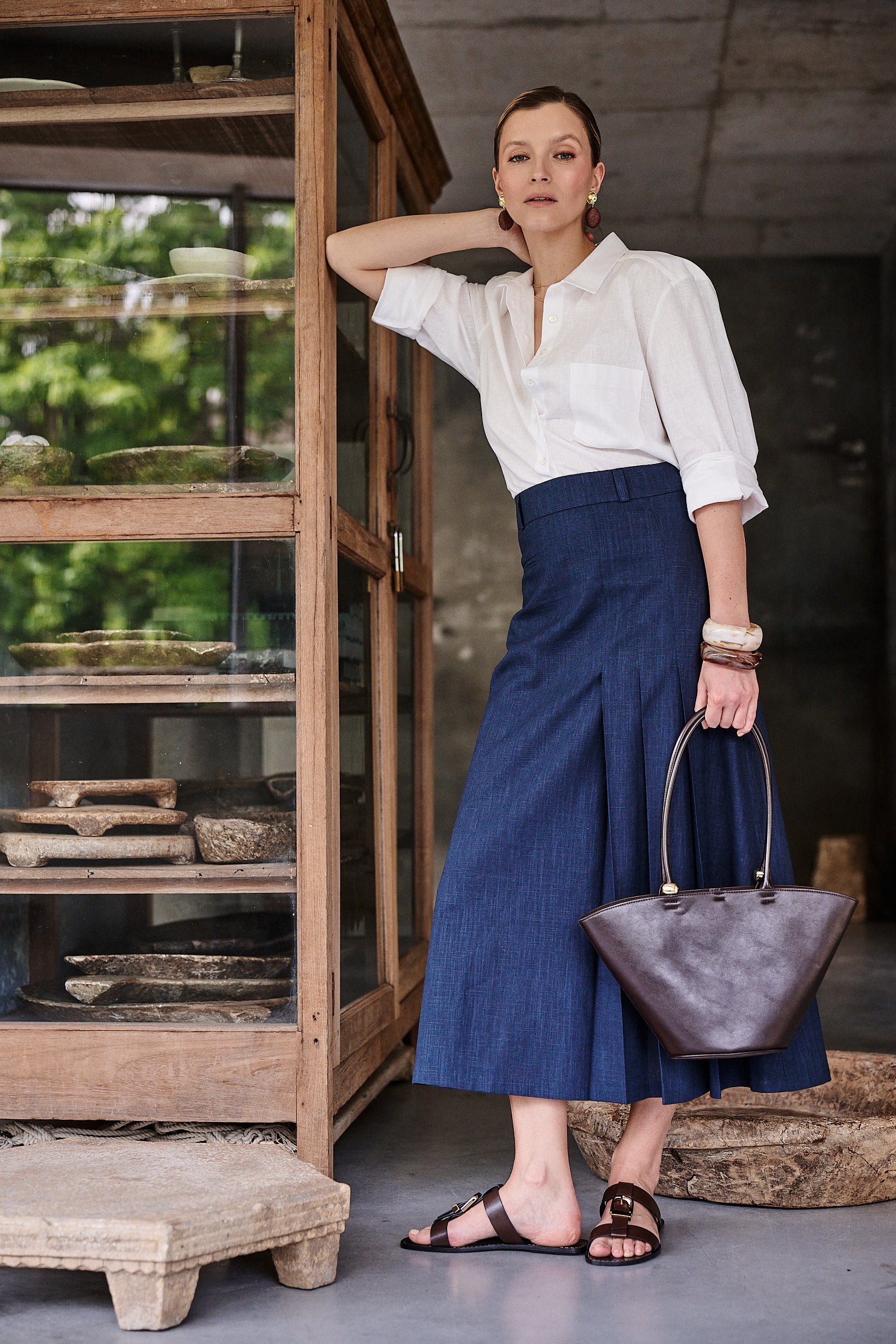 Spódnica Palermo Blu Marina od Aleksandry Markowskiej – lniana elegancja w głębokim odcieniu granatu, zestawiona z klasyczną białą koszulą i ciemnobrązową torebką, idealna na miejskie stylizacje.